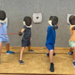 Synchroner Ausfallschritt von sechs Kindern nebeneinander während des Fechtcamps des UFC-Wien im Sommer.