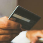Mann sitzt vor Laptop mit seiner Bankkarte in der Hand.
